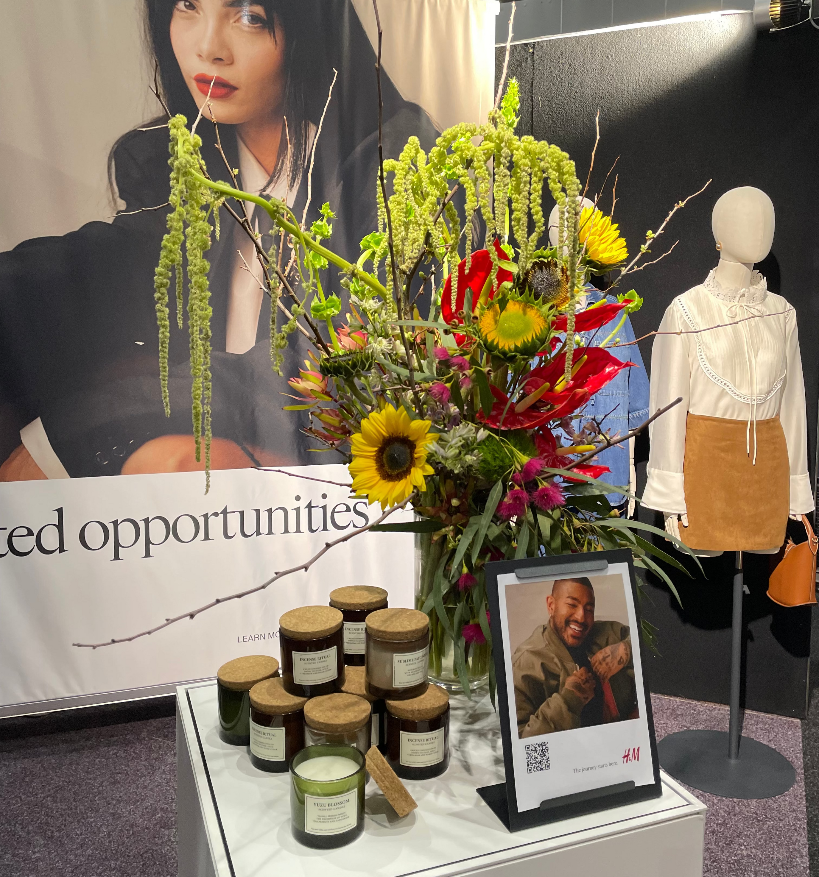 Display with flowers, candles, and a mannequin against a promotional backdrop.