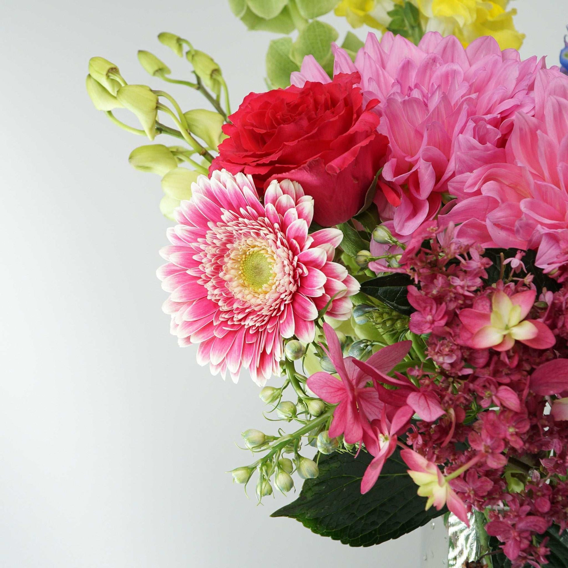 Colorful floral arrangement featuring delphinium, roses, dahlias, gerberas, snapdragons, hydrangea, and molucca balm in a vase. Colour Crush