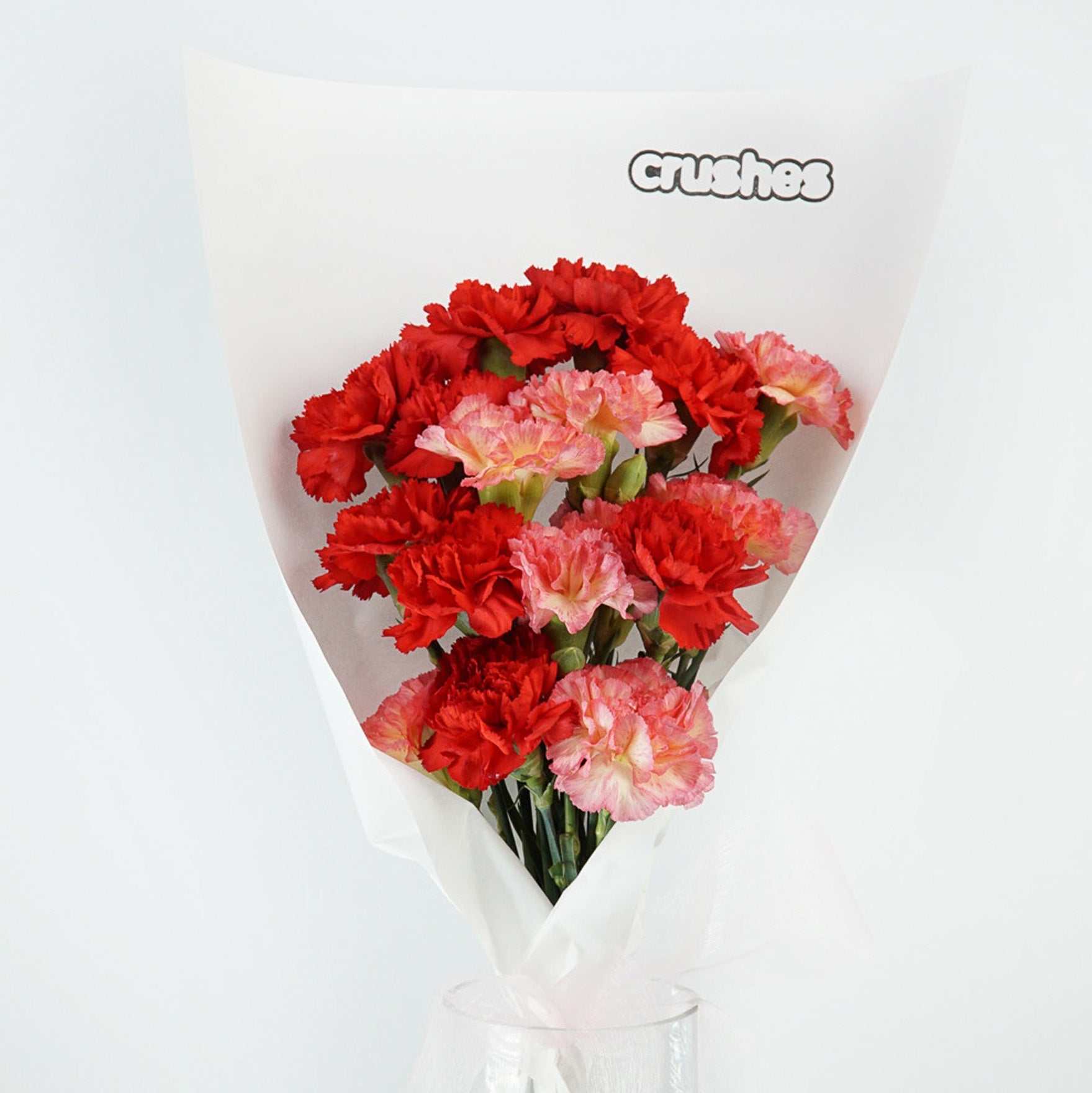 A bouquet of vibrant red and pink carnations wrapped in white paper labeled "Crushes".